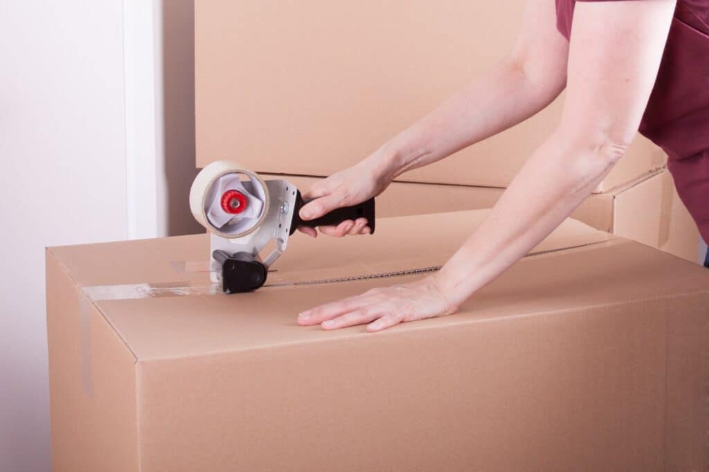 A woman sealing the cardboard box with a packing tape